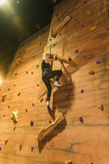 Woman scales indoor climbing wall at The Bear Grylls Adventure