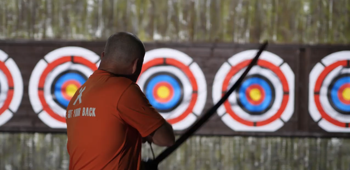 Man takes aim at target on archery range at The Bear Grylls Adventure