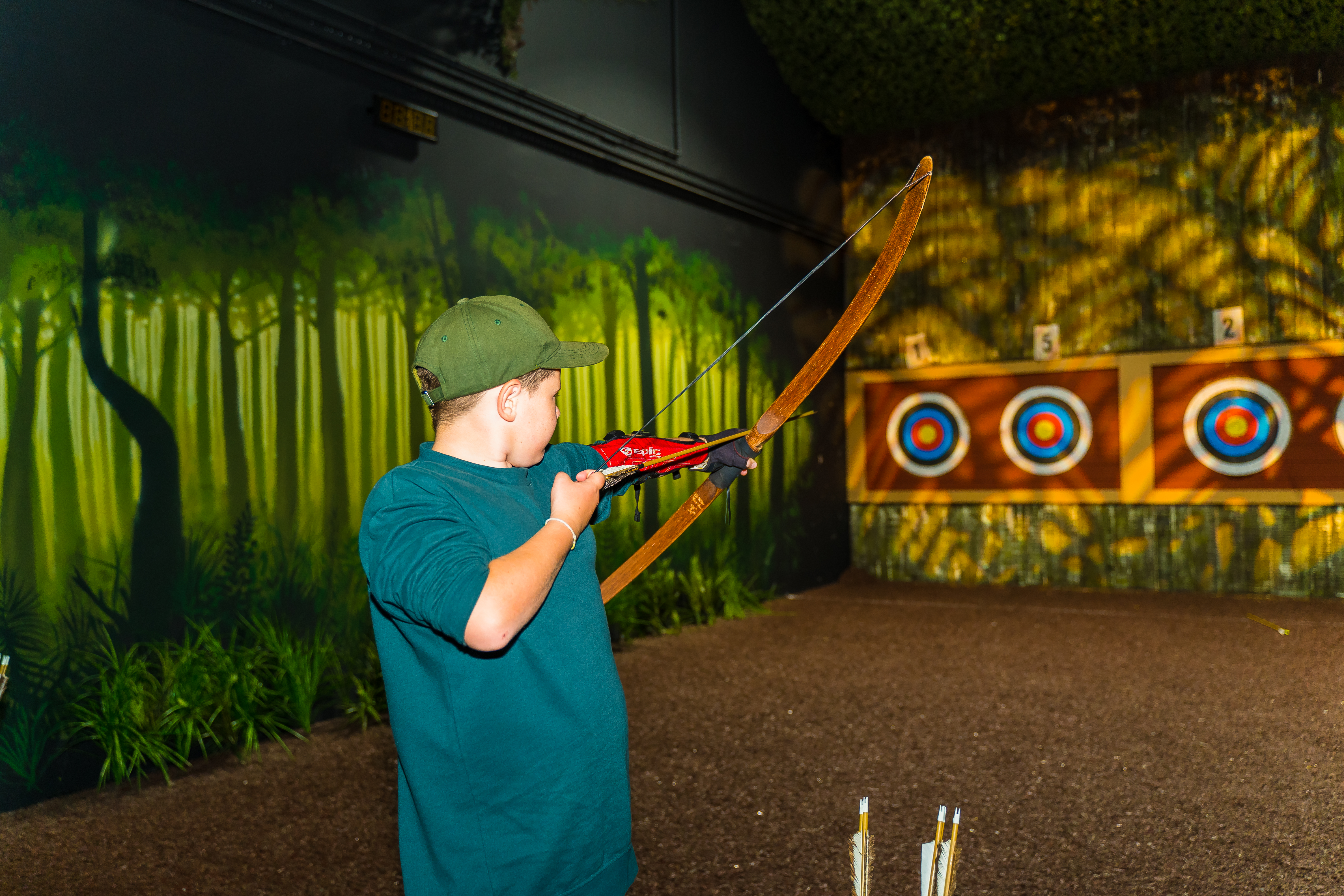Young boy takes aim at target on archery range at The Bear Grylls Adventure