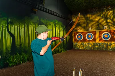 Young boy takes aim at target on archery range at The Bear Grylls Adventure