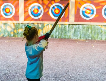 Young girl takes aim at target on archery range at The Bear Grylls Adventure